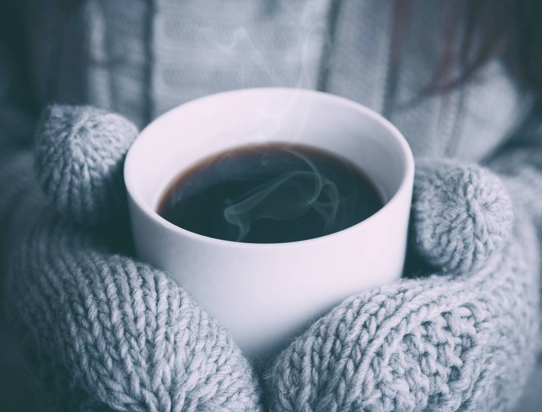 Person Holding A Hot Drink With Gloves On